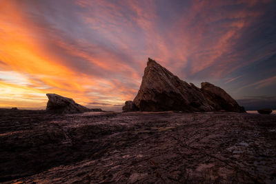 Rock formations on beach against sky during sunset
