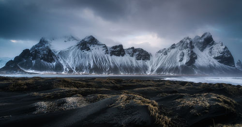 Panoramic view of snowcapped mountains by sea against cloudy sky