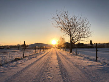 Snow covered field against sky during sunset