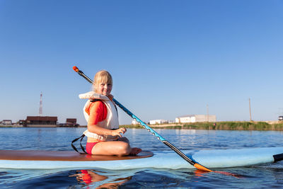 Rear view of woman surfing in sea against clear blue sky