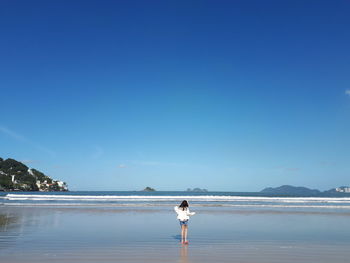 Girl standing at beach against blue sky