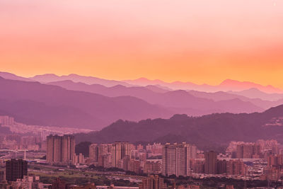 Aerial view of city by mountains against orange sky