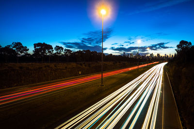 Light trails on road against blue sky at night