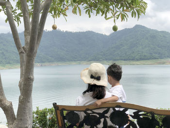 Rear view of mother and son sitting on bench at lake