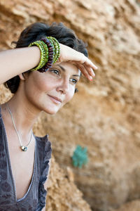 Close-up of smiling woman shielding eyes while looking away against rock