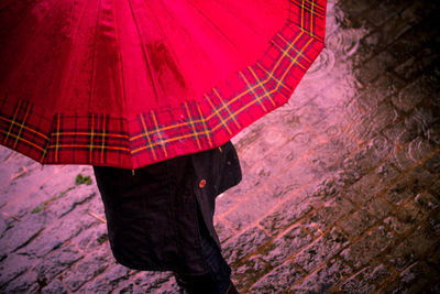 Person holding umbrella while standing on street during rainy season