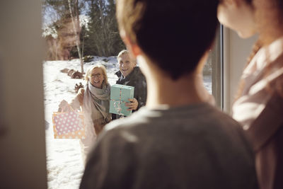 Siblings looking at happy grandparents through window