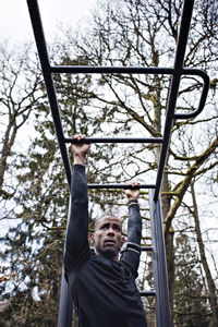 Low angle view of man exercising on monkey bars at outdoor gym