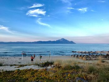 People at beach against blue sky during sunset