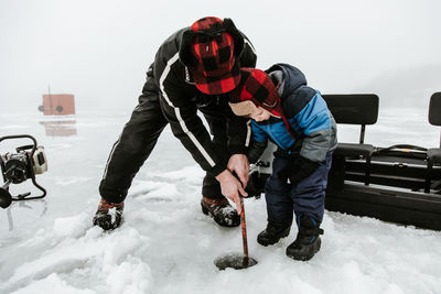 Senior man with grandson holding metal rod on frozen lake