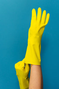 Cropped hand of woman wearing glove against blue background
