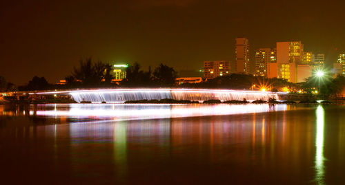 Illuminated buildings by river against sky at night