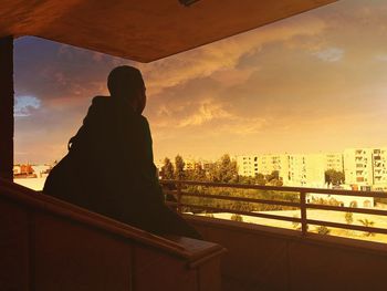 Rear view of silhouette man standing by cityscape against sky