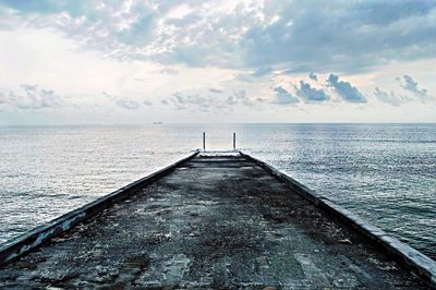 Pier on sea against cloudy sky