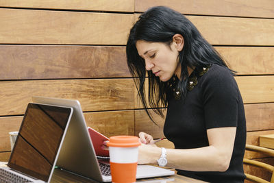 Side view of young woman using phone while sitting on table