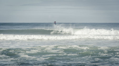 Mid distance view of person jumping while surfing in sea against sky