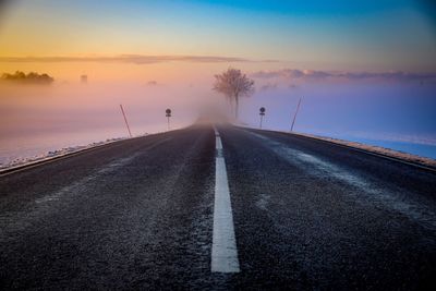 Road by sea against sky during sunset