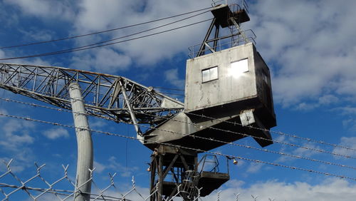 Low angle view of crane against cloudy sky