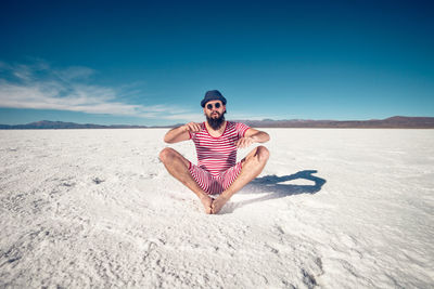 Full length of young man on sand in desert against sky