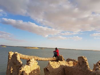 Woman sitting on rock by sea against sky