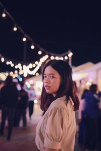 Portrait of young woman looking at illuminated city at night