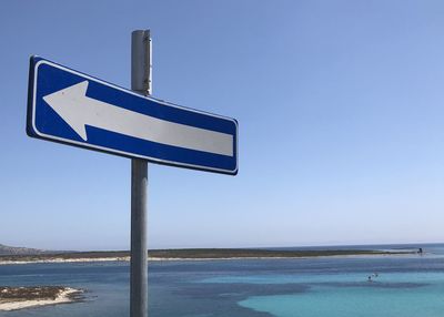 Information sign on road by sea against clear sky