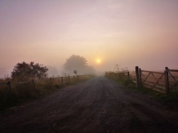 Road amidst field against sky during sunset