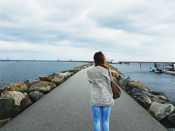 Rear view of woman walking on retaining wall by sea against sky