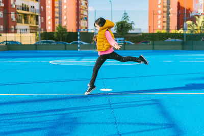 Girl jumping on blue sports court during sunny day