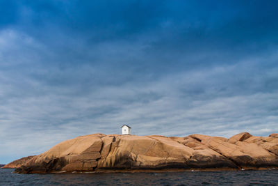 Lighthouse in sea against cloudy sky