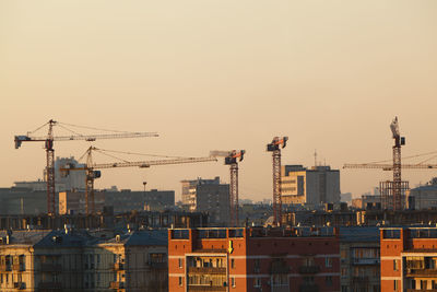 Buildings and cranes against sky during sunset