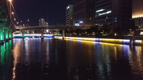 Illuminated bridge over river by buildings in city at night