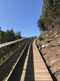 People walking on footbridge against clear blue sky