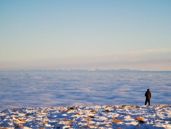 Man standing on snow covered land against clear sky during winter