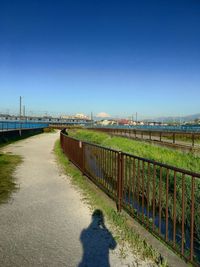 Walkway by sea against clear blue sky