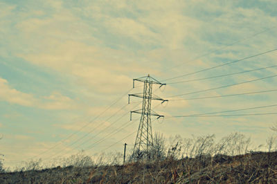 Electricity pylon on field against cloudy sky