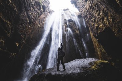 Rear view of woman standing on rock against waterfall