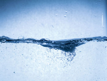 Close-up of water splashing on glass against blue background