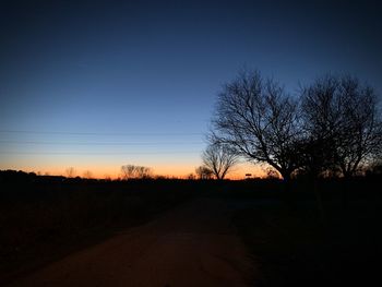 Silhouette bare trees on field against clear sky at sunset