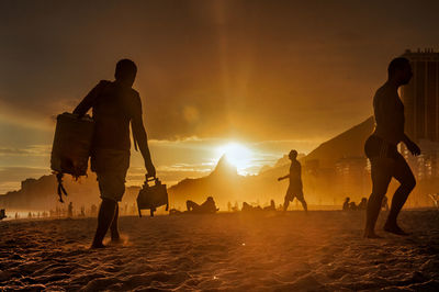 Silhouette people on beach against sky during sunset