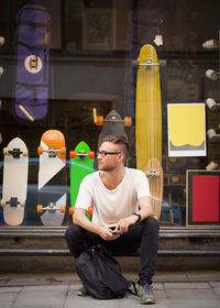 Full length of young man sitting outside skateboard shop