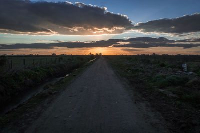 Road passing through field against cloudy sky