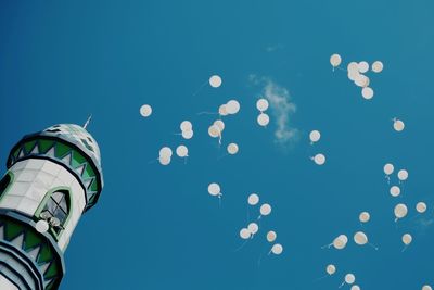 Low angle view of building by balloons against clear blue sky