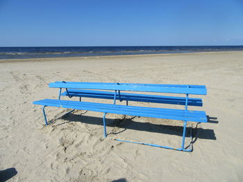 Empty deck chairs on beach against clear blue sky