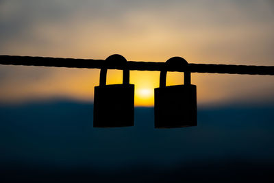 Close-up of padlocks hanging on metal pole against sky during sunset