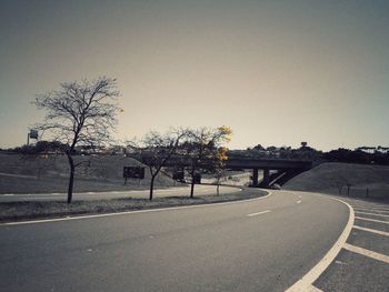 Empty road by trees against clear sky