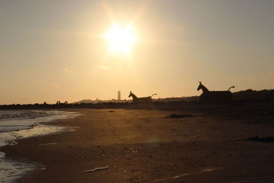 Silhouette horse sculptures at beach against sky during sunset