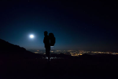 Silhouette man standing in illuminated city against sky at night