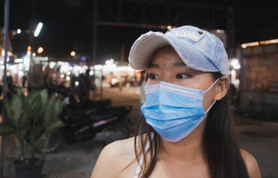 Close-up of young woman wearing flu mask and cap looking away standing outdoors