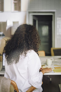 Rear view of female architect with curly hair working while sitting at office